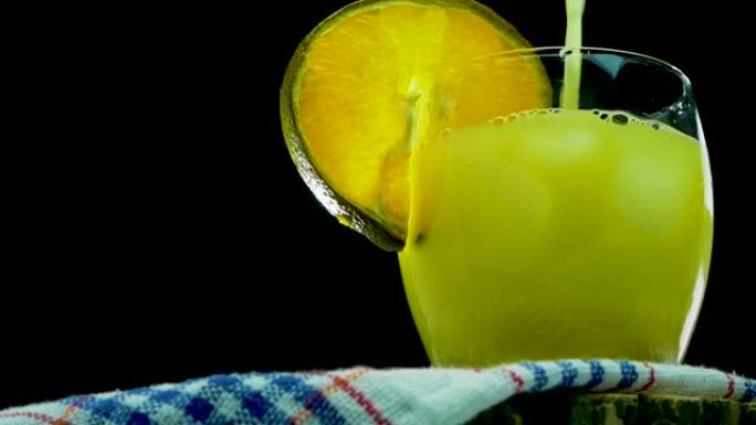 天然橙汁在玻璃杯中加入橙片，慢动作将黄色柠檬水倒入黑色背景上的玻璃杯中