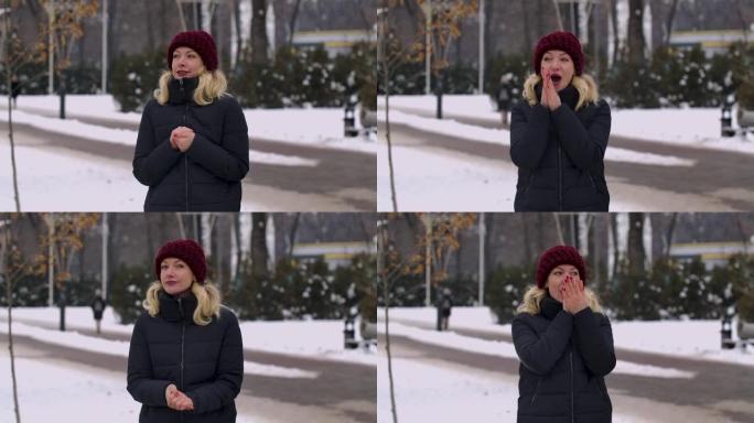 在寒冷的日子里，一个穿着冬装的女人站在公园中间。女孩忘记了她的手套，温暖了她的手，呼吸着它们，互相摩