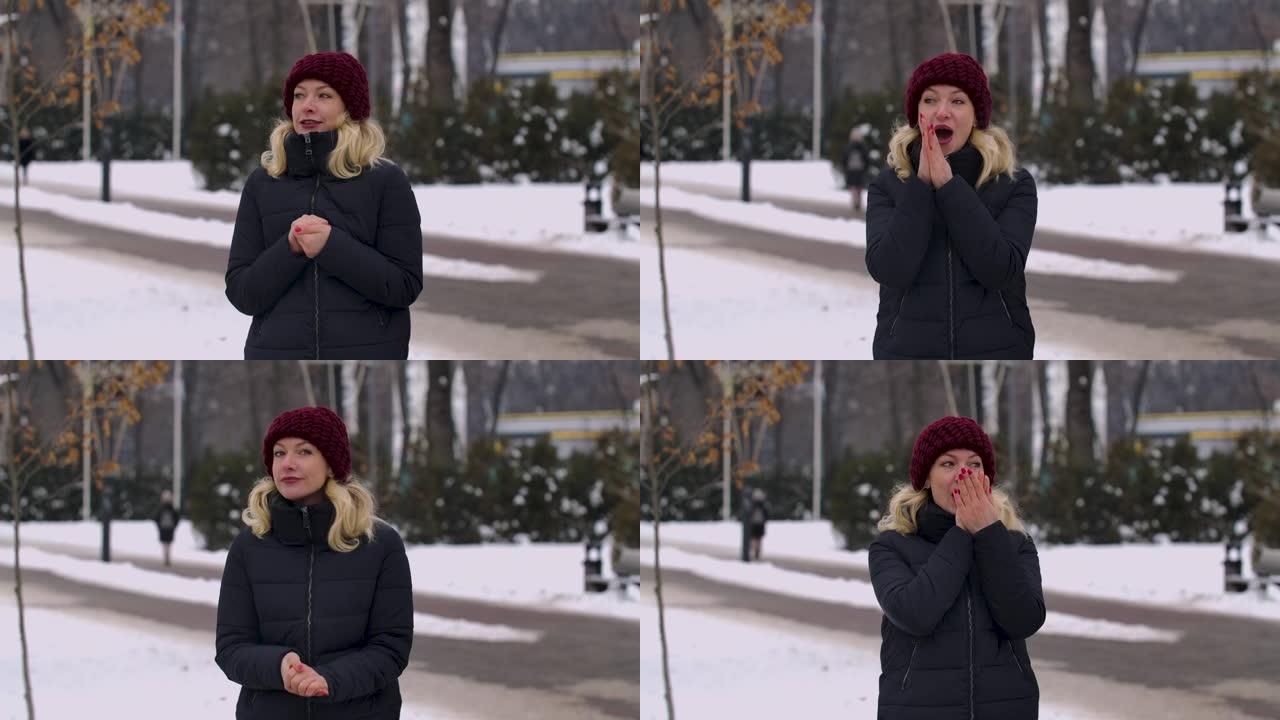在寒冷的日子里，一个穿着冬装的女人站在公园中间。女孩忘记了她的手套，温暖了她的手，呼吸着它们，互相摩