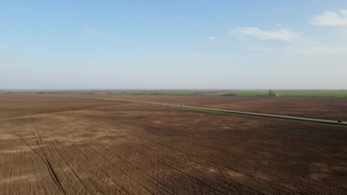 季节性收获后土壤松动的除草田地的全景。晴天，汽车沿着乡村道路行驶。带摄像头的无人机正以鸟瞰的高度在地