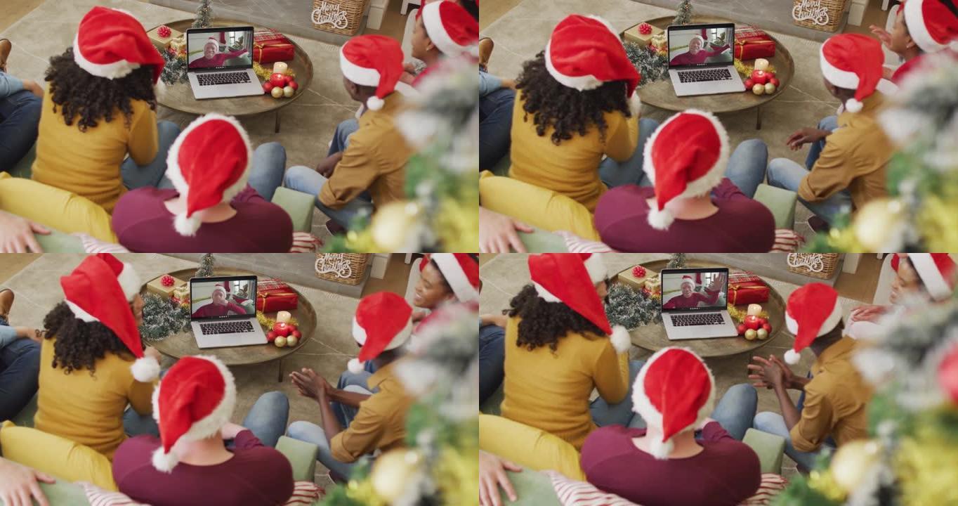 拥有圣诞老人帽子的多元化家庭使用笔记本电脑进行圣诞节视频通话，屏幕上有微笑的男人