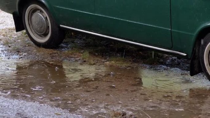 雨滴滴落在木头中自然停放的旧车附近的泥泞水坑中