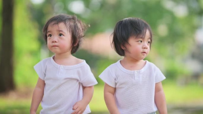 亚洲中国双胞胎男婴在周末娱乐活动中与他的兄弟在草坪公园指着并移开目光