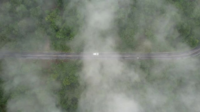 空中无人机电影拍摄的汽车和道路在早上下雨后越过山顶，有雾和绿色森林。