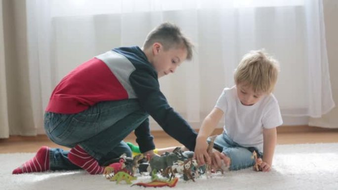 金发碧眼的孩子，蹒跚学步的男孩和他的哥哥preteeen男孩在家里玩塑料动物玩具