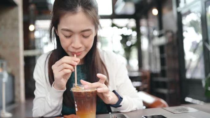 美丽的年轻亚洲女人喜欢在咖啡馆拍照，等她的朋友，喝咖啡，上传照片到社交网络微笑和开朗的脸真实的人