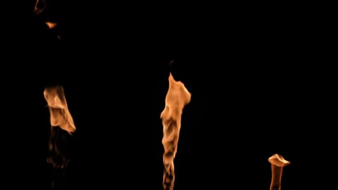 三个火焰交替点亮，并在黑色背景下发出橙黄色的火焰。真正的篝火、燃烧器或火炬在黑暗中燃烧起来。火光，危