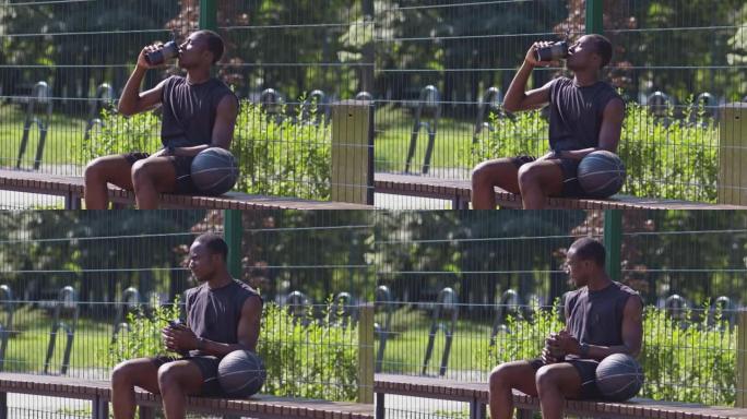 年轻的出汗的非洲裔美国运动员在长凳上休息和喝水，在街球比赛中休息