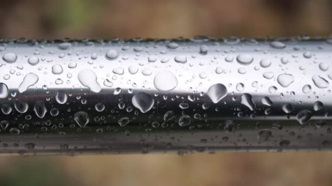 在模糊的海洋背景下，不锈钢扶手上的雨滴。特写镜头。雨露中的水滴聚集在闪亮的钢铬杆手轨栏杆上