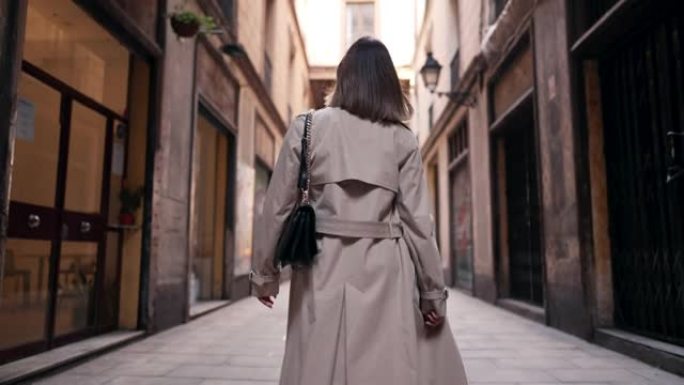 巴塞罗那哥特式区独自行走的女人的背影。旧公寓楼，欧洲狭窄的街道。秋天旅行，穿风衣的女士。
