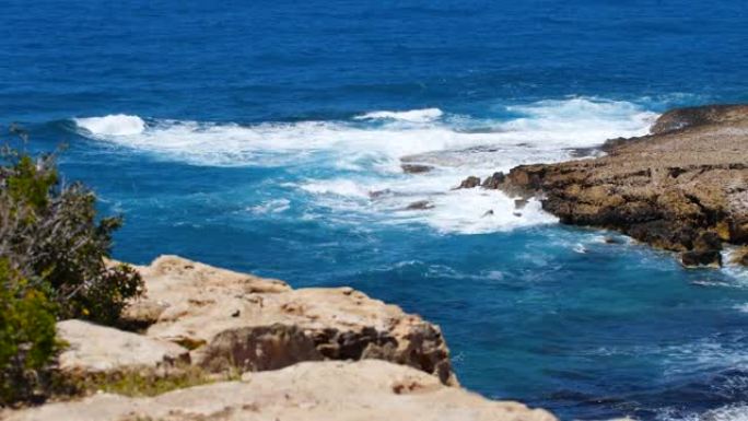 海蓝色的水和岩石的风景镜头，阳光明媚的白天海景，毁灭性的和壮观的，海浪在海岸的岩石上撞击，造成水的爆