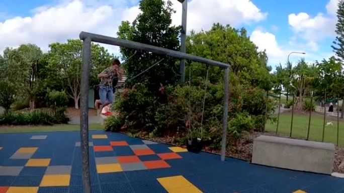 一个快乐的8岁男孩在昆士兰州阳光海岸的一个色彩缤纷的新公园里摇摆时微笑着。