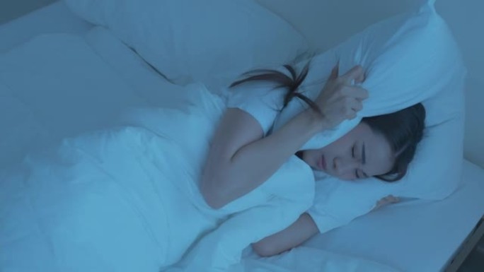 穿着睡衣的亚洲美丽沮丧的女孩在黑暗的夜晚睡在床上。迷人的年轻女子躺着，由于噪音而感到沮丧和愤怒，并在