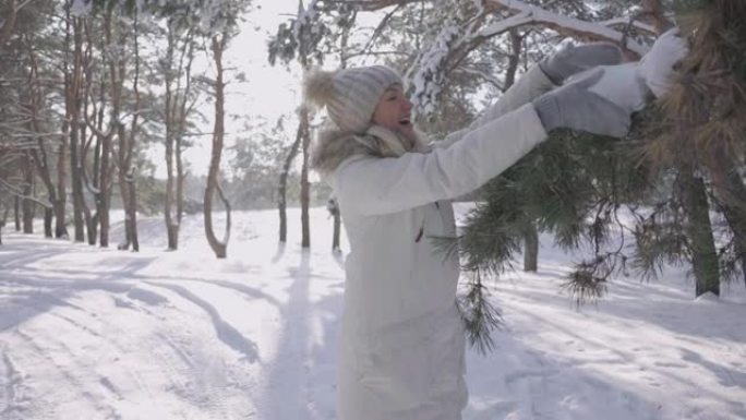穿着冬衣和帽子的可爱女孩抚摸着白雪覆盖的松树枝，开心地微笑着。松树上的雪。晴天在冬天的白雪皑皑的森林