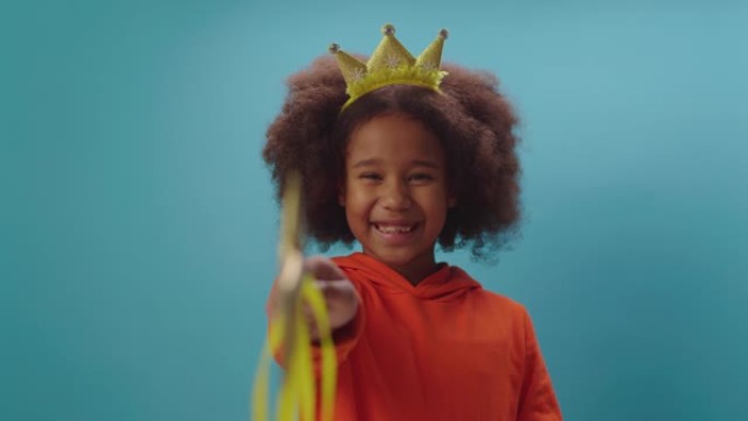 戴着皇冠的可爱的非洲裔美国女孩拿着魔杖看着相机。微笑的女孩扮演仙女。让魔法开始。
