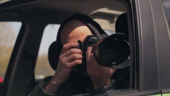一名男子坐在汽车上，用专业相机，私人侦探或狗仔队间谍拍照。