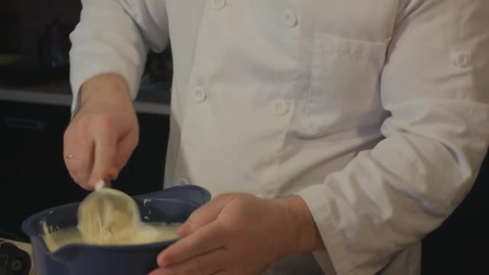 男糕点厨师用搅拌器搅打完奶油，轻敲碗上剩余的奶油，然后取出搅拌器
