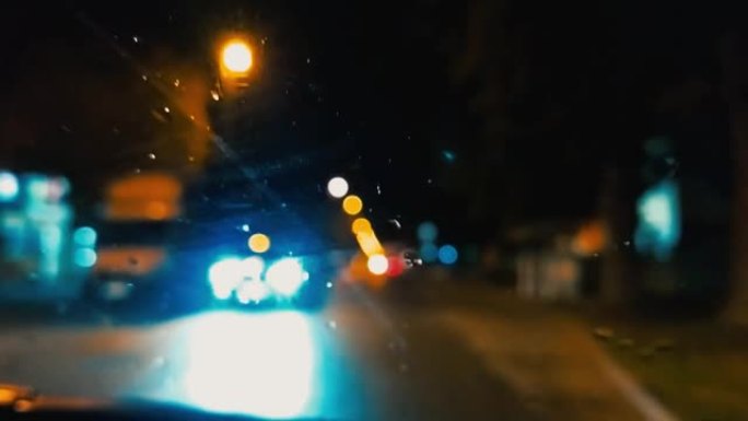 晚上的交通。雨滴在汽车挡风玻璃上。柏油路或轨道。模糊和散焦效果。专注于玻璃上的液滴。夜灯、汽车、路标