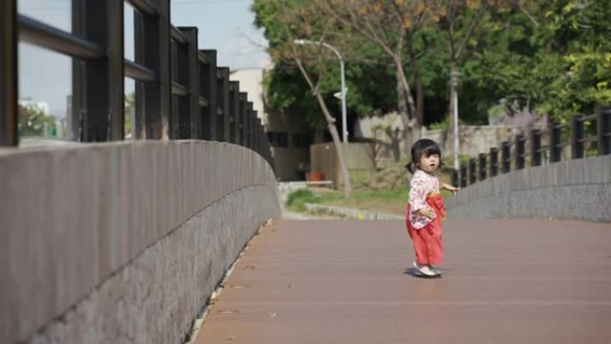 在阳光明媚的日子里，一个穿着女式和服，精力充沛的日本幼童为了继续在公园的桥上玩耍，时而跌倒，时而爬起