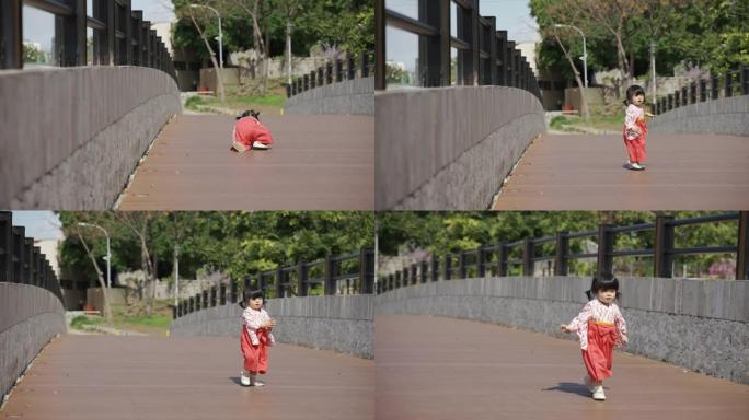 在阳光明媚的日子里，一个穿着女式和服，精力充沛的日本幼童为了继续在公园的桥上玩耍，时而跌倒，时而爬起