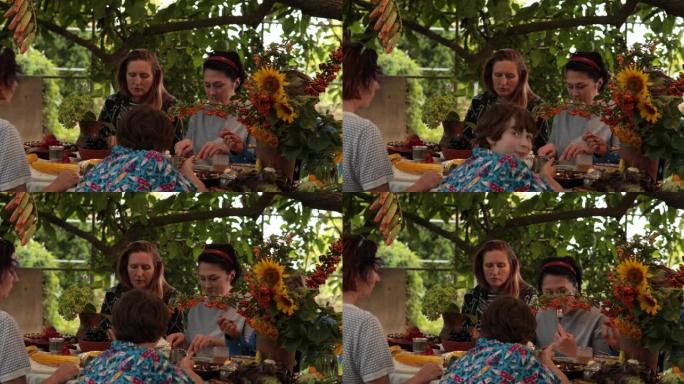 妇女和10多岁男孩在秋季花园聚会上的感恩节晚餐上吃饭