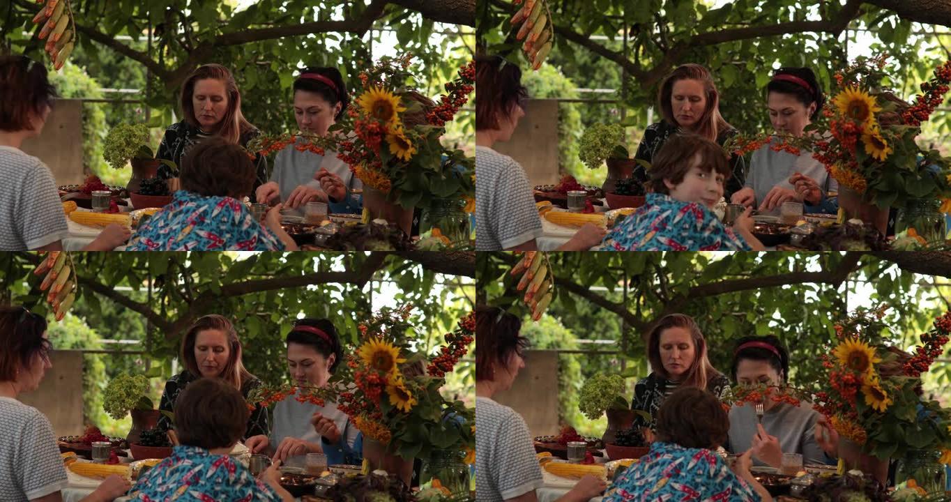 妇女和10多岁男孩在秋季花园聚会上的感恩节晚餐上吃饭