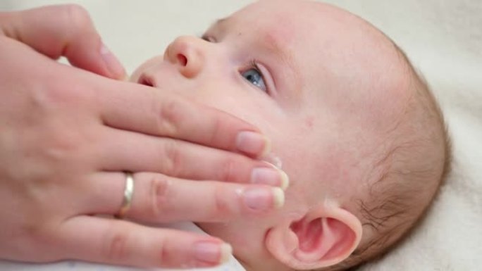 母亲的手在患有痤疮和皮炎的小婴儿的皮肤上涂抹保湿医用乳液的特写镜头。新生婴儿卫生、健康和皮肤护理的概