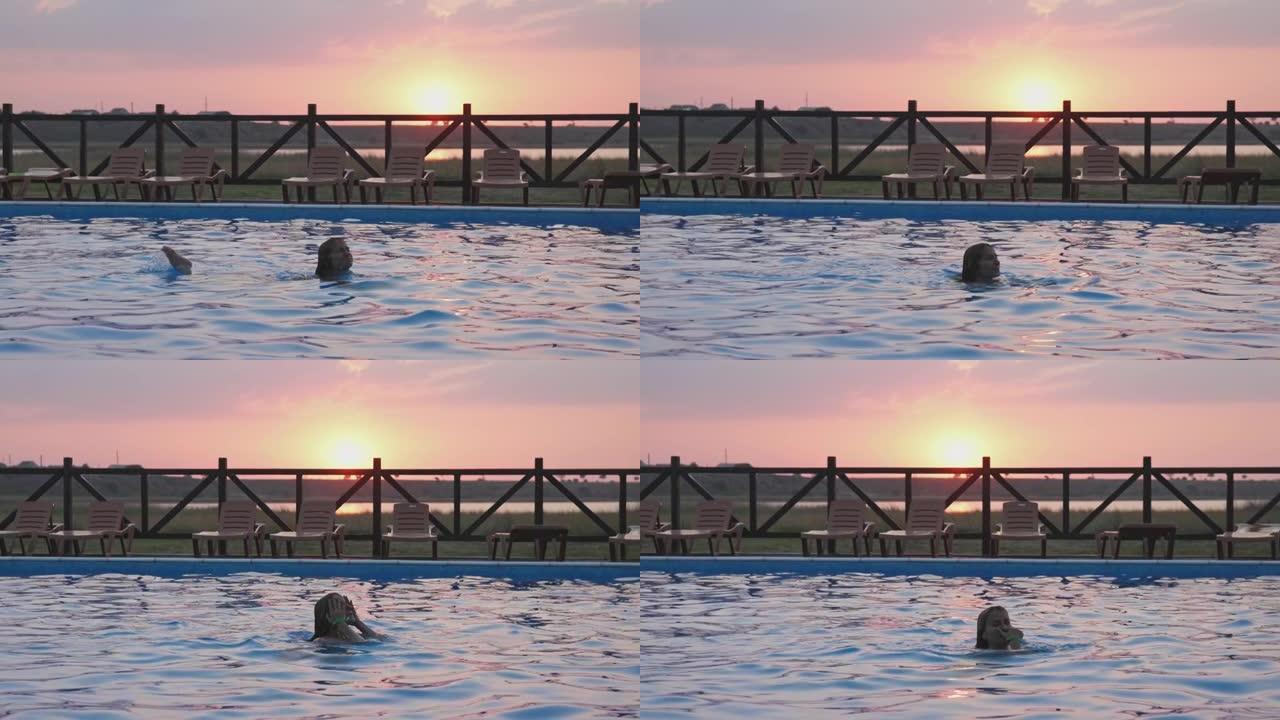穿着彩色比基尼的湿头发的女孩在夏天日落的背景下从透明清水的游泳池里出来
