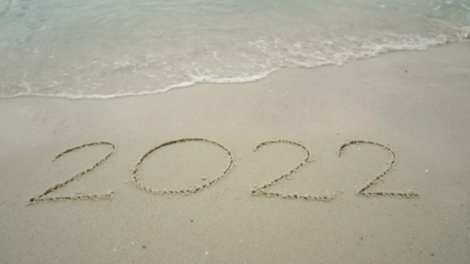 4k快乐新2022年。数字2021写在沙滩上，海浪飞溅变化2022年。新年快乐倒计时从2021年20