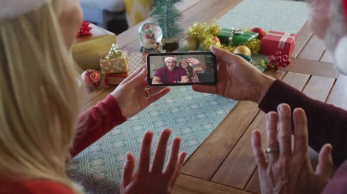 戴着圣诞老人帽子的高加索夫妇使用智能手机进行圣诞视频通话屏幕上的夫妇