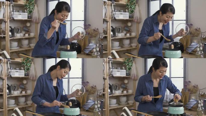 尝试从锅中品尝美味汤的亚洲女性对味道感到满意，并在将盖子放回家里的厨房之前先将汤匙上的液体沥干。