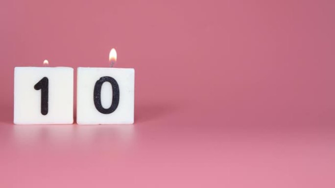一根方形蜡烛，上面写着数字10在庆祝生日或周年纪念日的粉红色背景上被点燃和吹灭