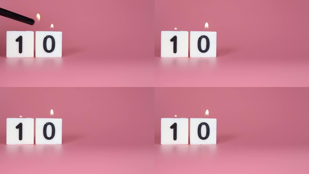 一根方形蜡烛，上面写着数字10在庆祝生日或周年纪念日的粉红色背景上被点燃和吹灭