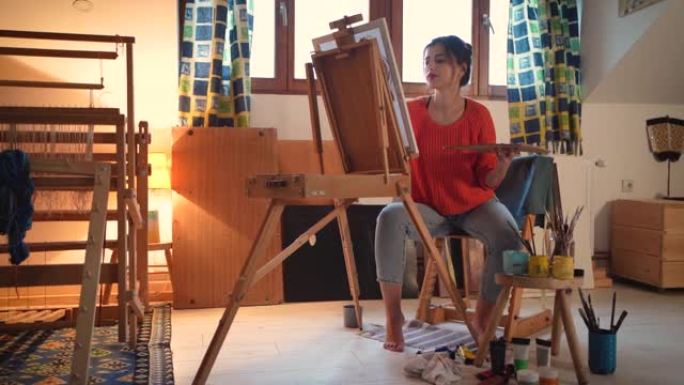 在她舒适的艺术工作室里，高加索女艺术家在画布上绘画