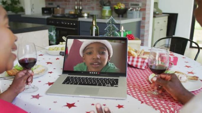 非裔美国人夫妇与葡萄酒使用笔记本电脑与屏幕上的男孩进行圣诞节视频通话