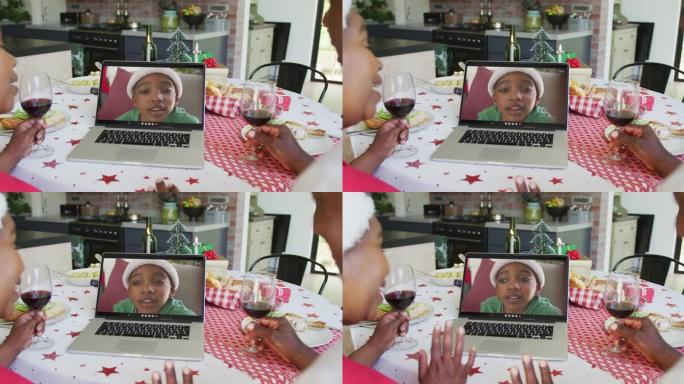 非裔美国人夫妇与葡萄酒使用笔记本电脑与屏幕上的男孩进行圣诞节视频通话