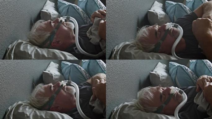 睡眠呼吸暂停的成熟男子在床上睡觉时戴着CPAP面罩