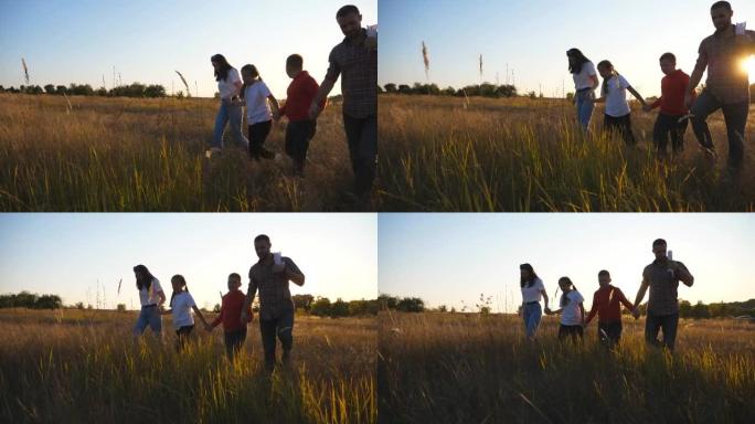带着小孩的年轻父母在日落时手牵着手穿过草地。妈妈和爸爸带着两个孩子去夏日草地，一起享受大自然。多莉开