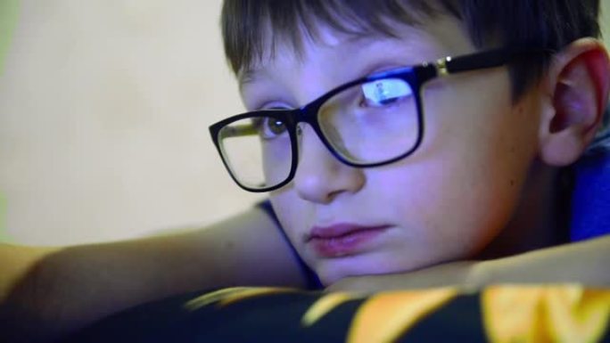 一个戴着眼镜的男孩脸的特写。孩子看着笔记本电脑屏幕或显示器的屏幕