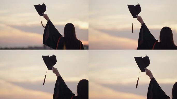 毕业于大学的女学生站在日落的户外时间，毕业于剪影日落概念。