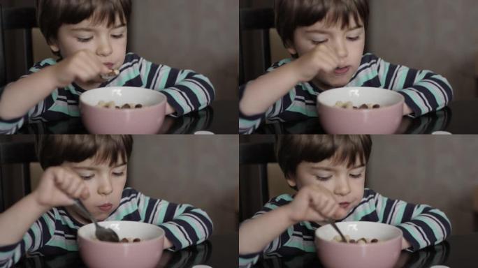 孩子吃玉米片和牛奶。饥饿的小男孩坐在厨房的餐桌上，从盘子里吃早餐玉米麦片。健康营养薄片。早餐吃早餐的