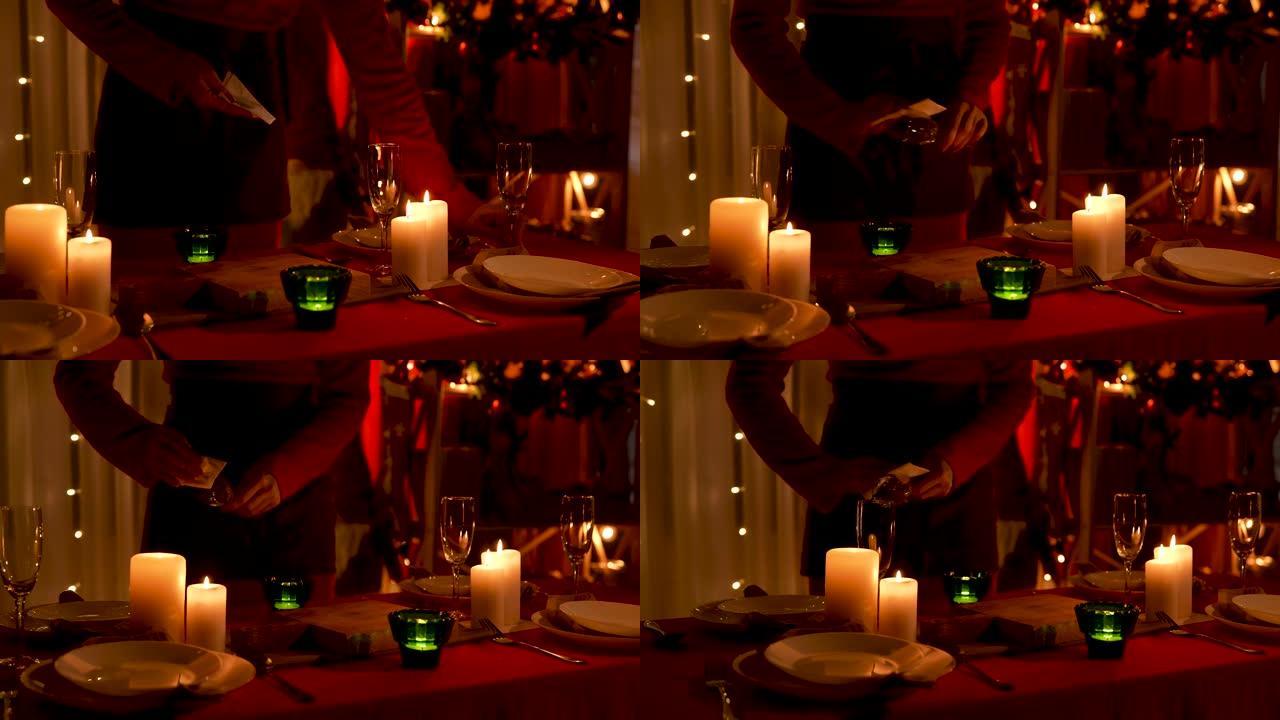 女人在装饰新年或圣诞节的房间背景下擦拭香槟杯。节日餐桌上的蜡烛正在燃烧。光线不足。双手合拢。慢动作