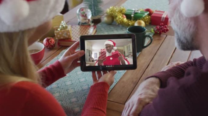 带有圣诞老人帽子的高加索夫妇使用平板电脑进行圣诞视频通话屏幕上的圣诞老人
