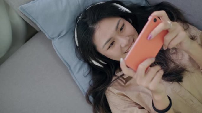 年轻的亚洲女性在家中使用智能手机玩电子竞技