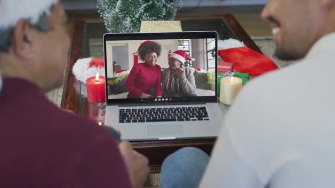 带有圣诞老人帽子的混血儿父子使用笔记本电脑与家人在屏幕上进行圣诞节视频通话