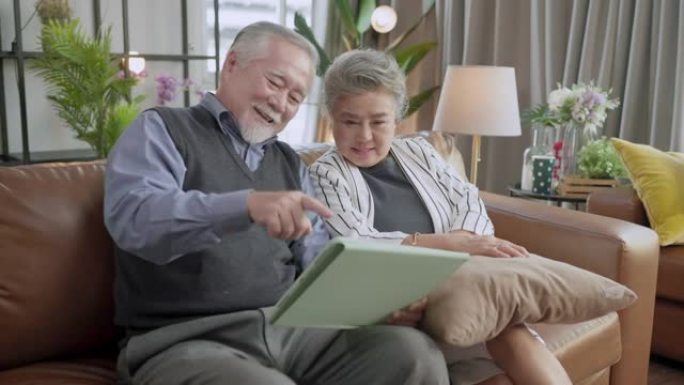 老亚洲老年夫妇退休年龄坐在沙发沙发上视频用平板电脑给家人打电话社交连接家庭隔离呆在家里国家秩序概念，