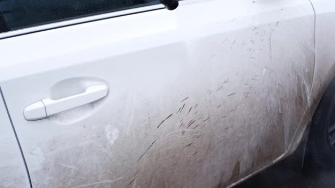 自助洗车店的白人妇女使用带有温水和底盘洗发水的高压清洗机洗掉白色车辆上的污垢和泥土，产生活性泡沫的雾