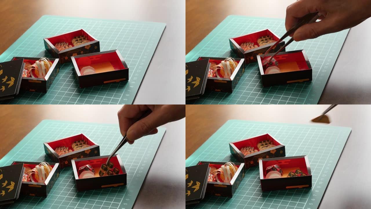 用镊子捏纸制osechi餐具，并将其放在沉重的盒子中。