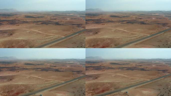 通过沙质沙漠山谷的道路上的无人机鸟瞰图和附近的汽车用石块组成