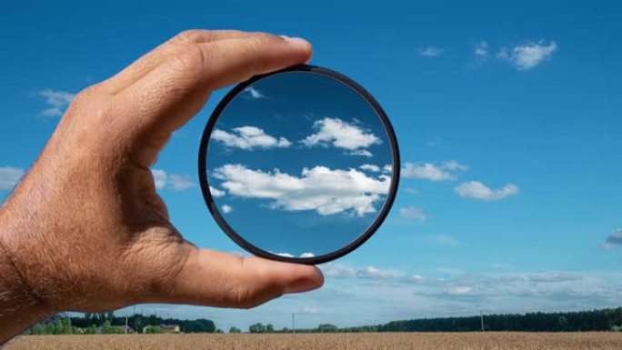 偏光滤镜的视觉效果以夏季乡村美丽的云彩为例。手握一个圆形滤光片，应用偏振效应。